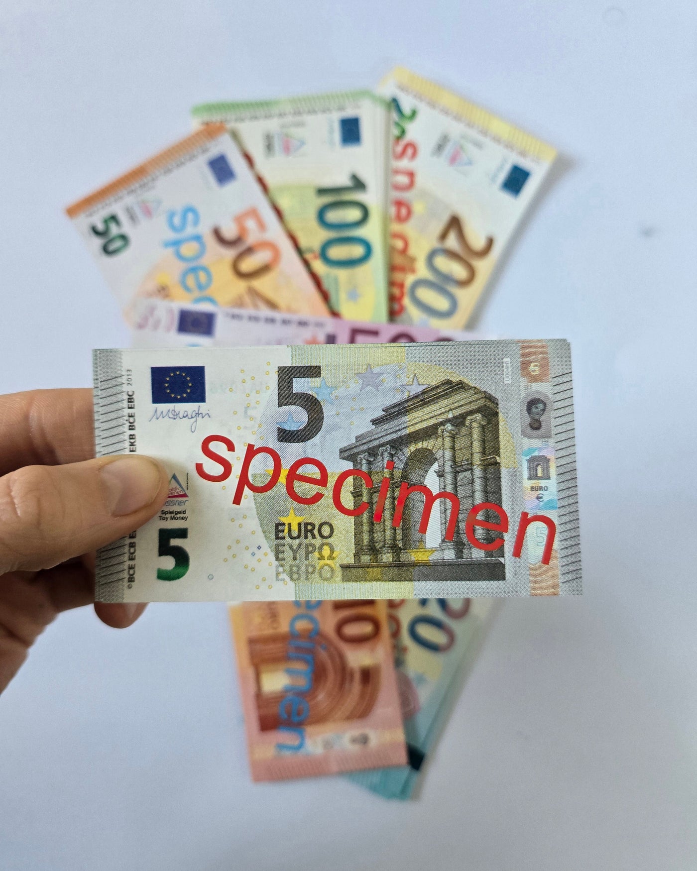 Kuvassa tuotepaketin sisältö, niin että kädessä pidetään 5 euron seteleitä pinossa ja muut setelit näkyvät taustalla.