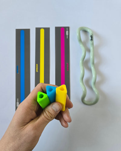 Kuvassa tuotepaketin tuotteet eli kolme lukuliuskaa, tangle ja kolme kynätukea. Kynätuet on henkilön kädessä ja muut tuotteet taustalla.